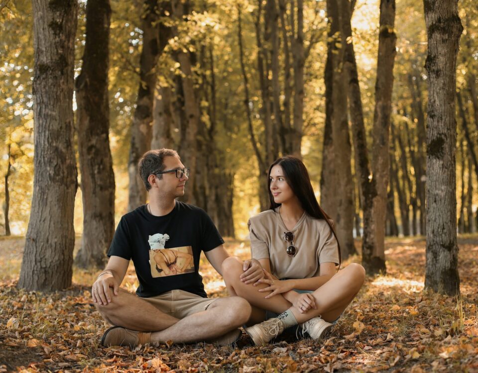 a man and a woman sitting on the ground in a forest
